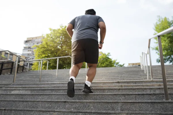 Fot ter illustratie bij de ketenaanpak gecombineerde Leefstijl Interventie voor volwassenen. Op de afbeelding is een volwassene met overgewicht te zien op de rug. Hij is aan het joggen en gaat een brede stenen trap op.