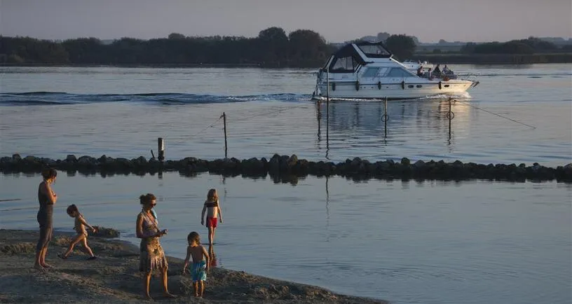 Bootje op een meer en mensen aan de kant van de wal bij zonsondergang